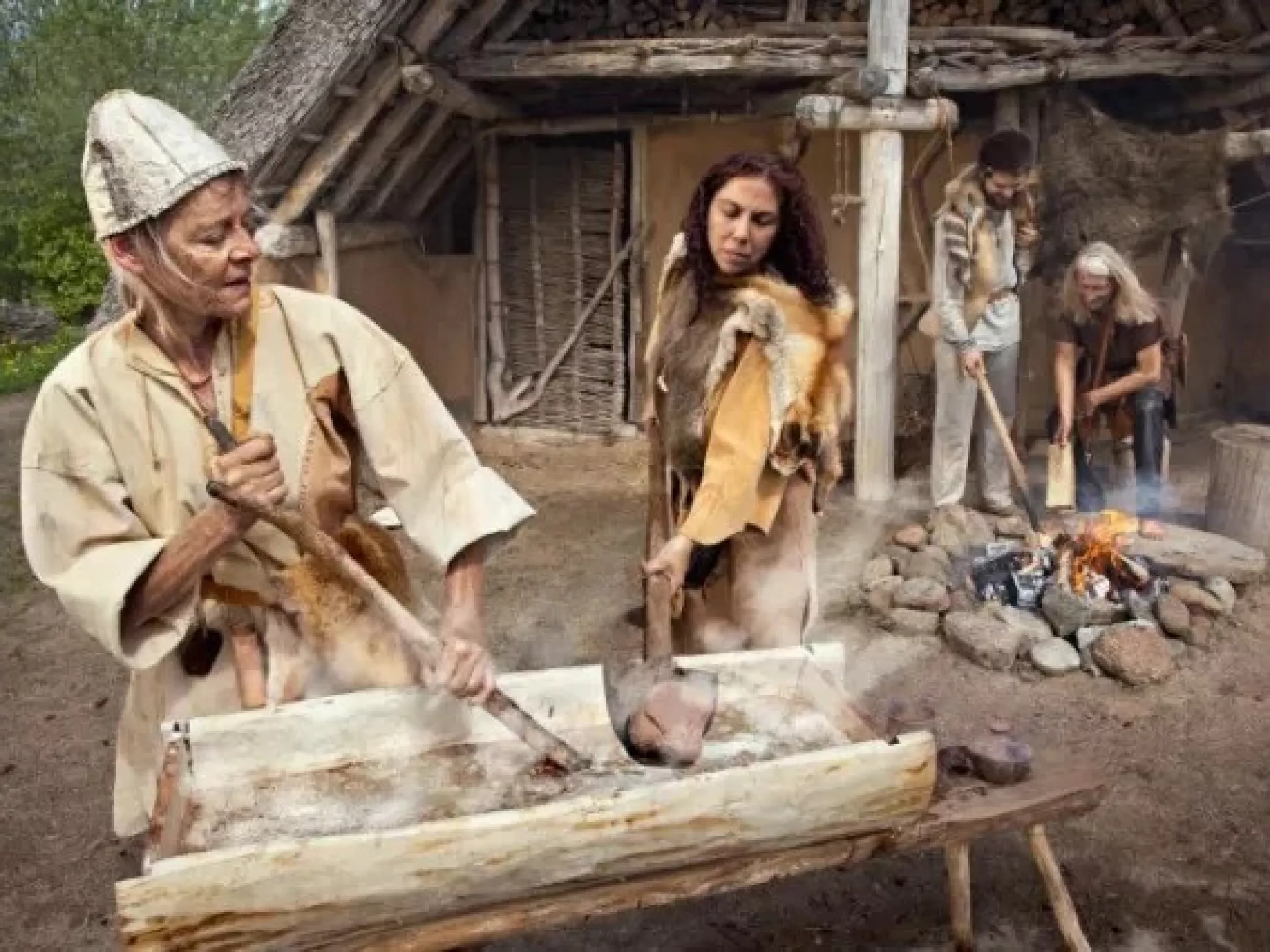 Mensen in historische kleding bereiden voedsel in een rustieke omgeving.