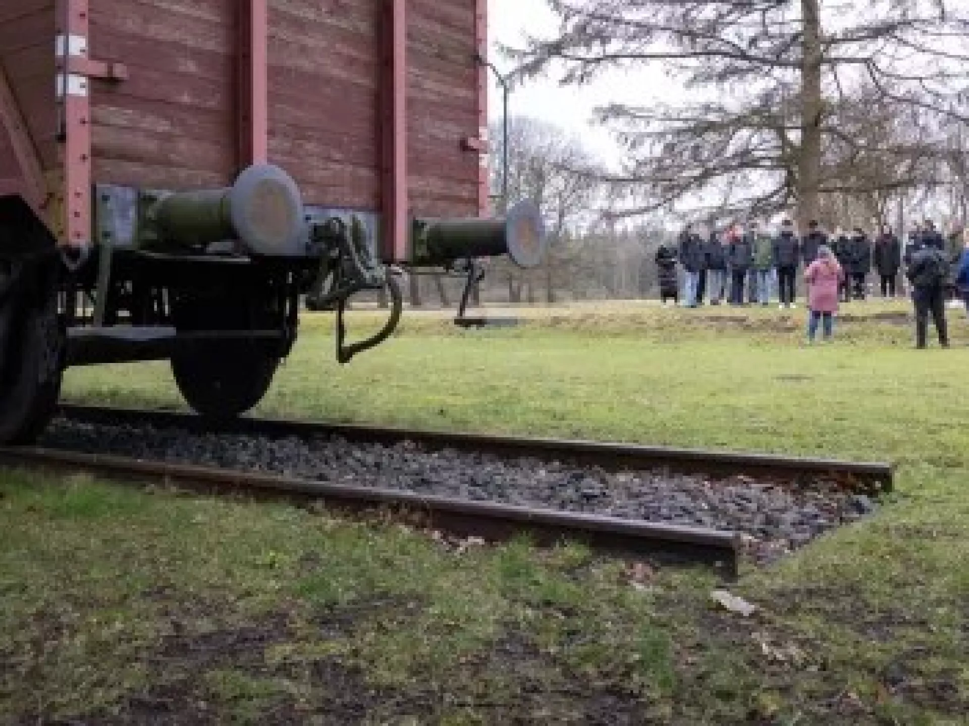 Een groep mensen verzameld bij een oude treinwagon op een grasveld.