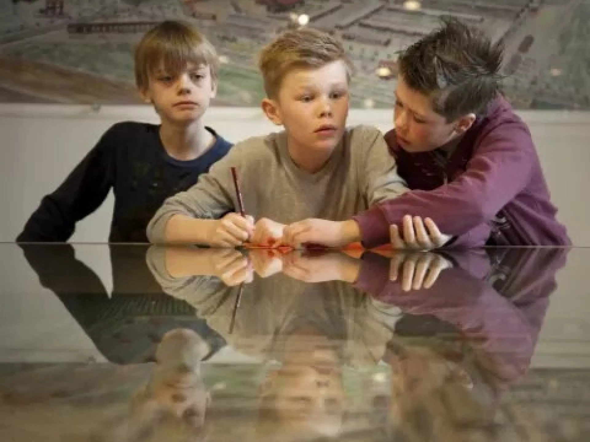 Drie jongens zitten samen aan een tafel, bezig met een potlood.