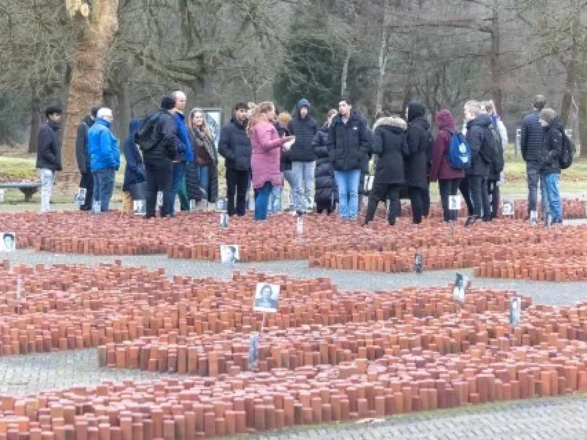Groep mensen verzameld bij een monument met foto's en bakstenen.