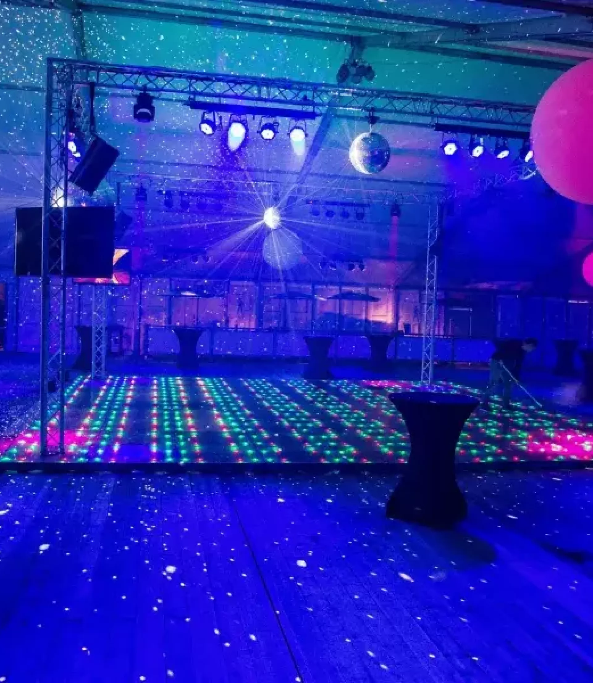 Verlichte dansvloer met kleurrijke ballonnen en sfeerverlichting in een feestlocatie.