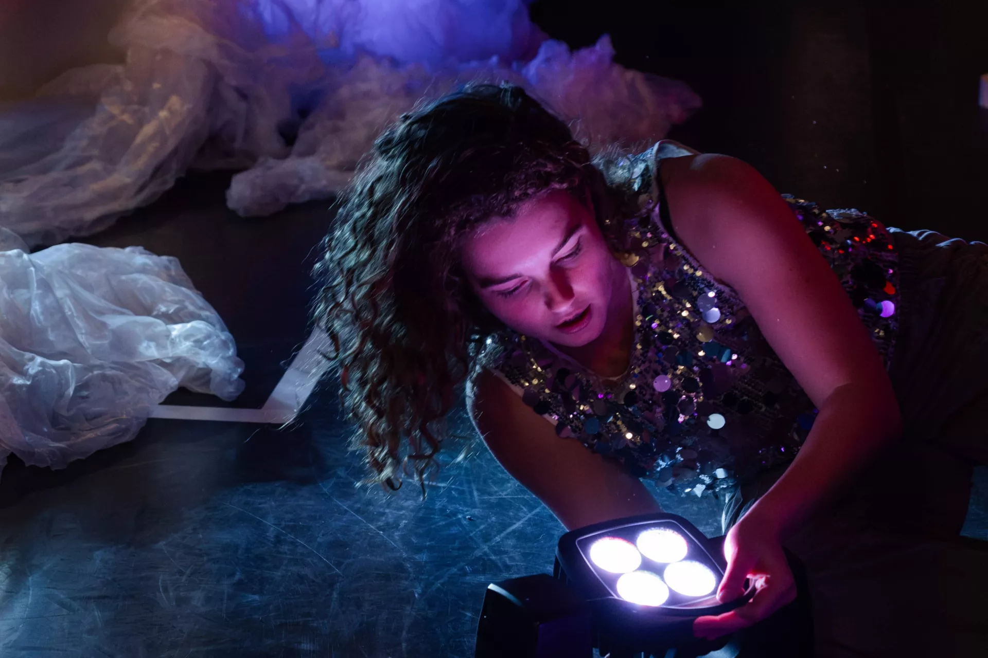 Vrouw onderzoekt een kleurrijke lamp in een donkere ruimte.