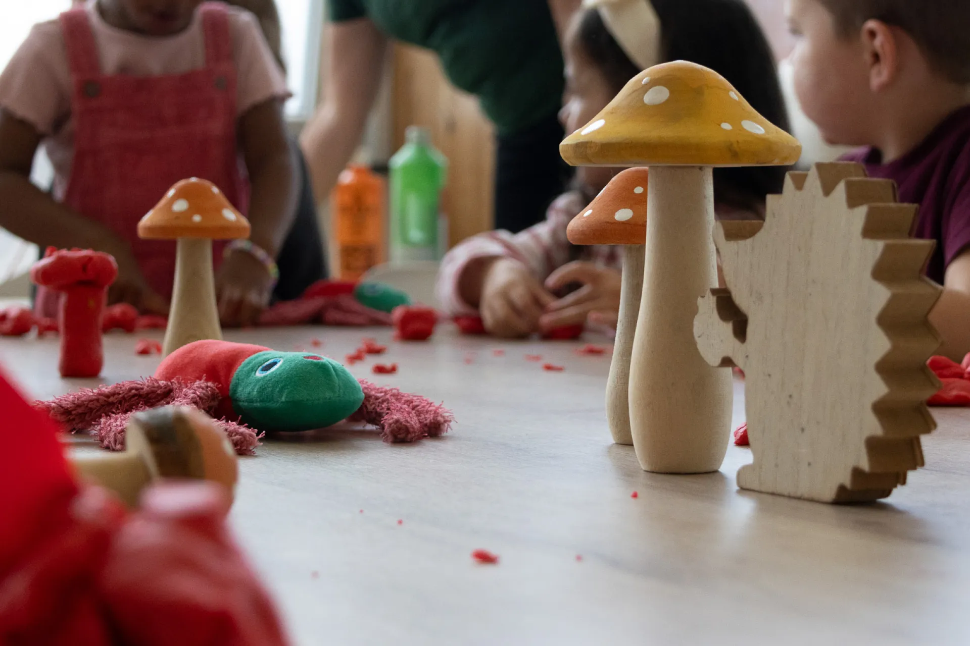 Kinderen spelen met klei en houten paddenstoelen op een tafel.