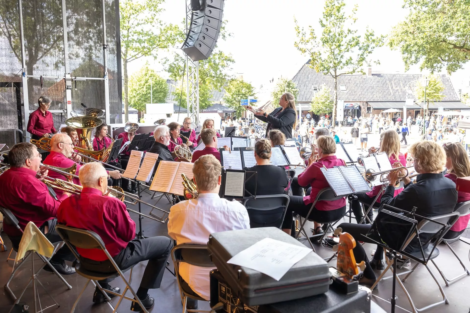 Je ziet een orkest vanaf het podium op een zonnige dag. In de verte zie je het publiek kijken.